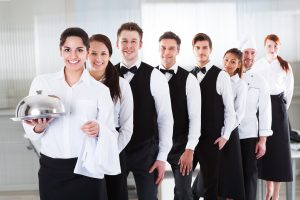 Waiters and waitresses in white tops and black pants stand in a line.