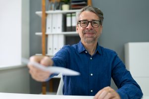 A man in a blue button-down shirt holds out a blurred-out paycheck.