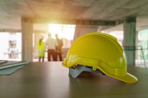Picture of a yellow hard hat on a table with people in the far background.
